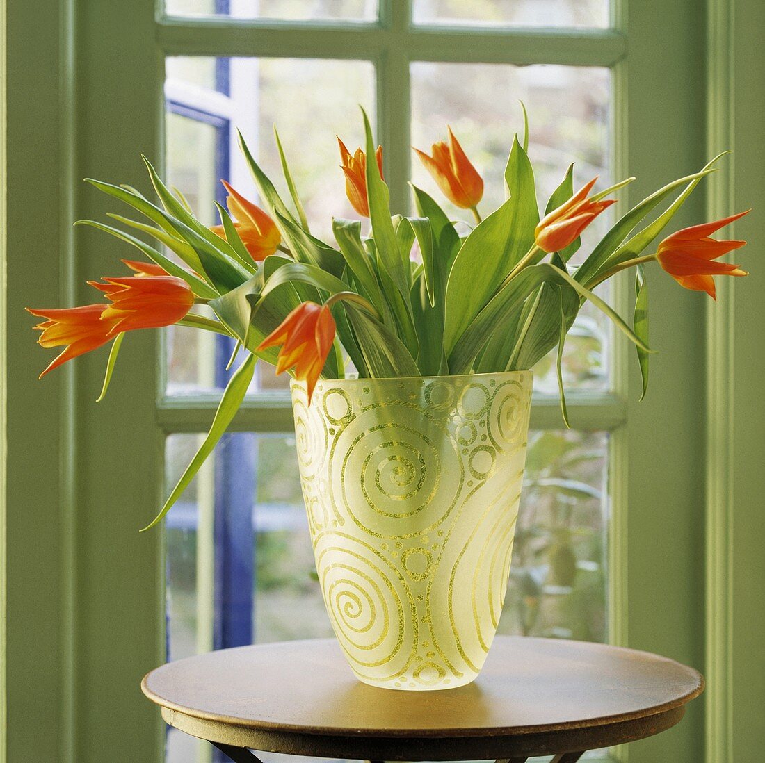 Orangefarbene Tulpen in einer Glasvase mit Gravur auf einem kleinen Holztisch