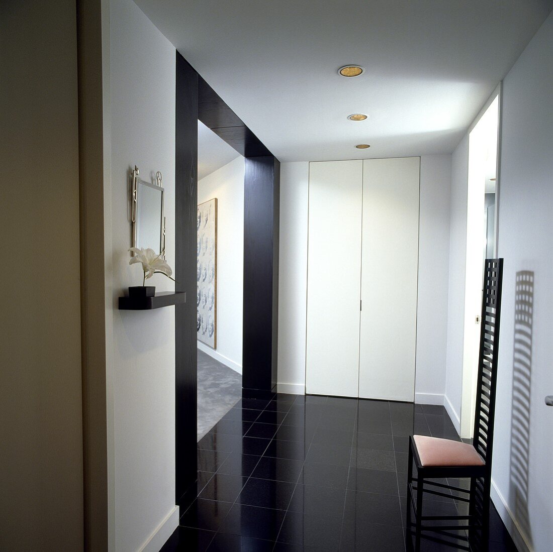 Diele mit schwarzem Fußboden, modernem Stuhl, weissen Wänden und einem weissen Einbauschrank