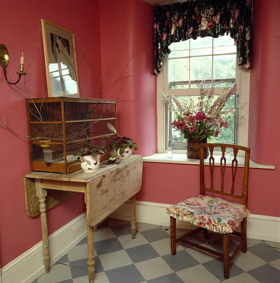 Landhauszimmer mit antikem Vogelkäfig auf einem Holztisch und antikem Stuhl mit Blumenkissen
