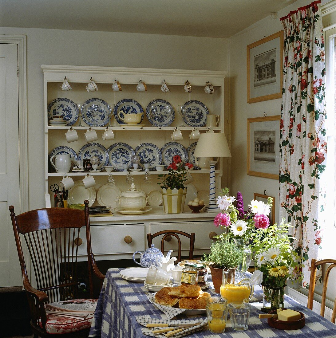 Esszimmer mit weißem Küchenbuffet mit blau-weissen Porzellantellern, gedecktem Frühstückstisch und einer karierten Tischdecke