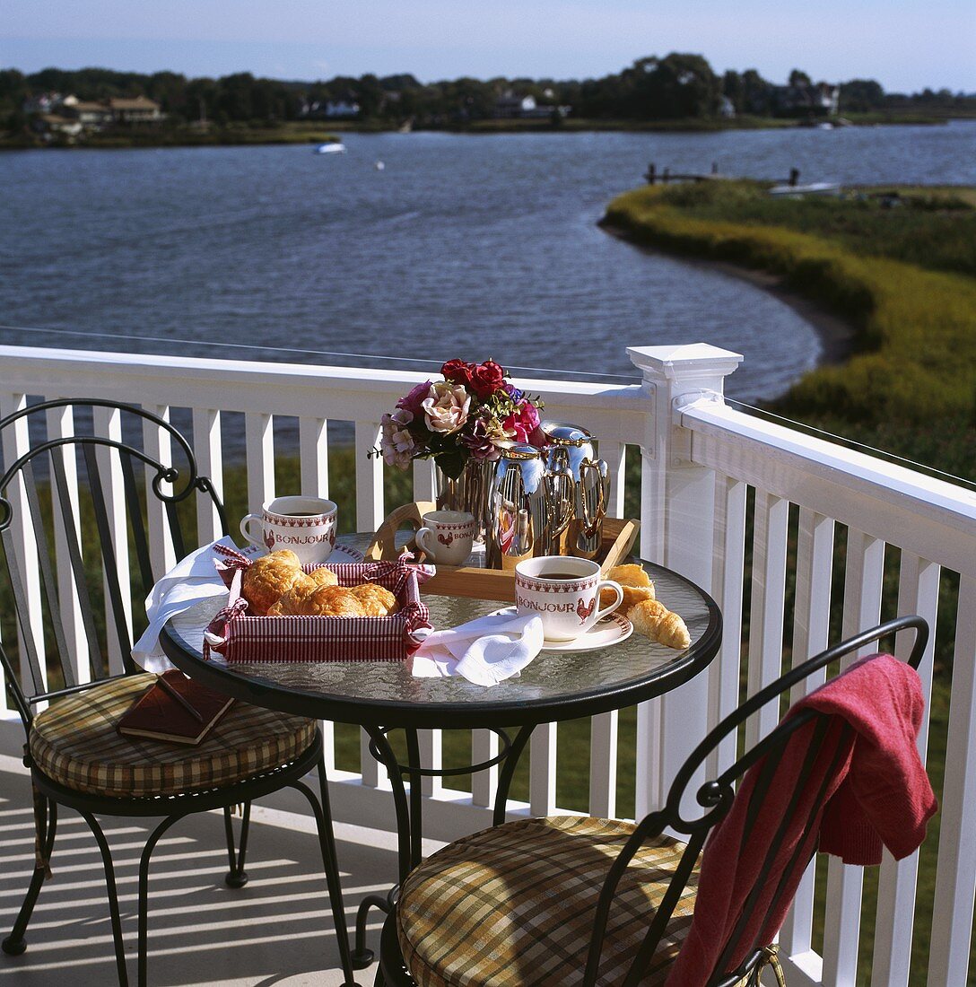 Zwei Metallstühle und ein kleiner Frühstückstisch auf dem Balkon mit Blick auf einen Fluss