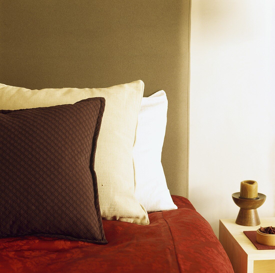 Brauen und cremefarbene Kissen und rote Decke auf dem Bett mit gepolstertem Kopfteil aus Wildleder