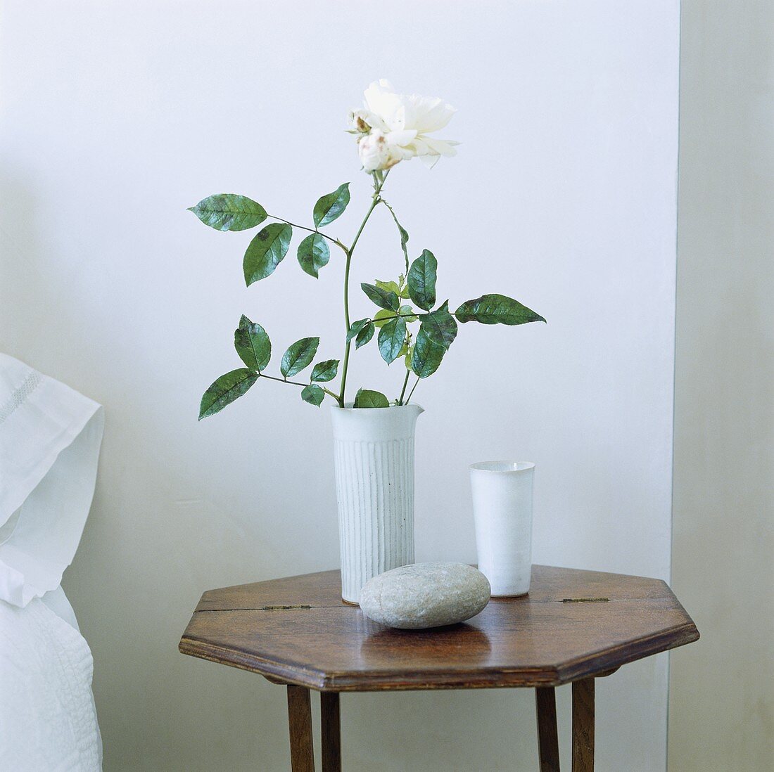 weiße Rose in einer Keramikvase auf einem achteckigen Beistelltisch aus Holz