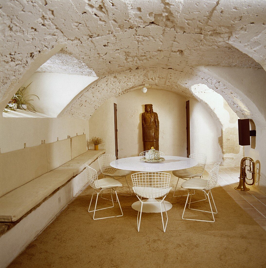 weiße Saarinen-Tisch, Eames-Stühle und Sitzbänke in einem Esszimmer im Keller mit rauer Steindecke