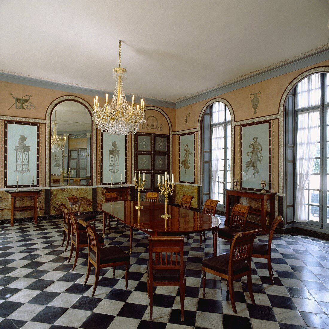 Kronleuchter über antikem Tisch und Stühlen, gewölbte Spiegel und Fenster in einem Esszimmer mit Schachbrettmuster-Boden