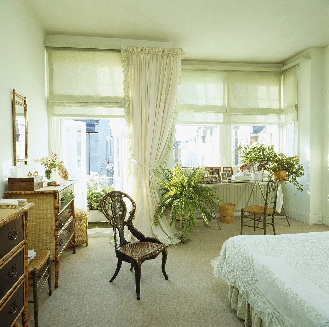 Antiker Intarsien-Stuhl und cremefarbener Teppichboden in einem weissen Schlafzimmer mit grünen Vorhangrollos und weissen Vorhängen