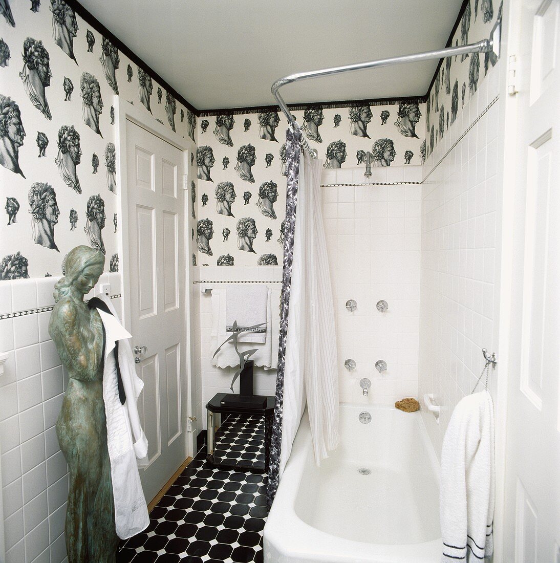 Schwarz-weiße Tapete mit Kopf-Muster und eine Statue in einem monochromatischen Badezimmer