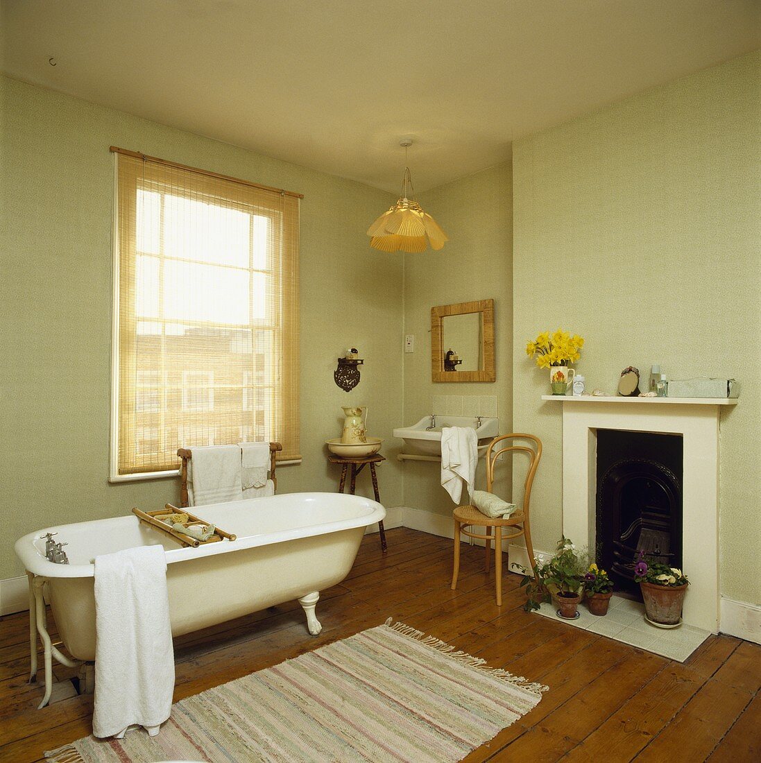 Ein lindgrünes Badezimmer mit Holzboden, Kamin und einer frei stehenden Badewanne vor dem Fenster