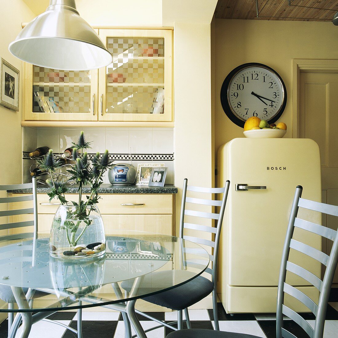 Runder Glastisch mit Metall-Stühlen und ein frei stehender Kühlschrank in einer cremefarbenen Küche