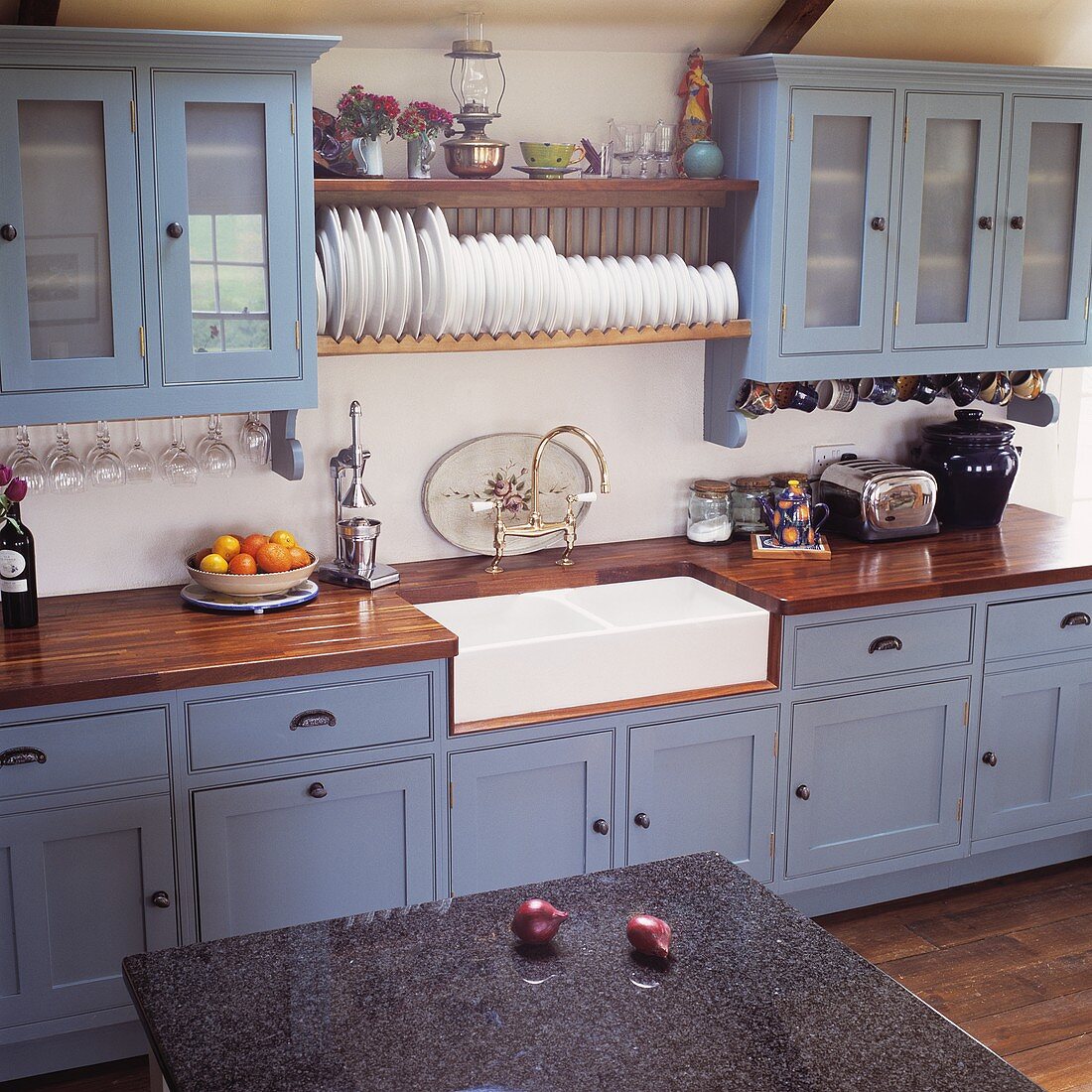 Landhausküche mit blaugrauen Fronten und Küchenboard mit Tellern über weisser Keramikspüle
