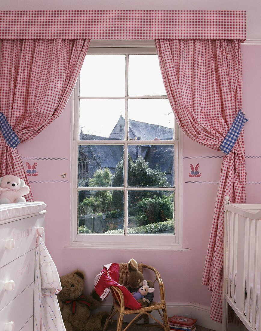 Rot weiss karierte Vorhänge neben Sprossenfenster darunter Rattanstühlchen mit Spielsachen im Kinderzimmer