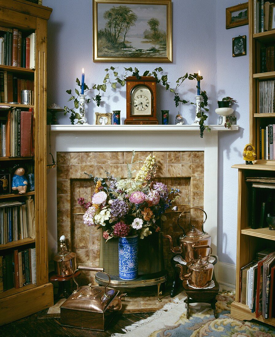 Blumenstrauss und Kupferteekessel vor Kaminraum und weißem Sims in Bibliotheksecke