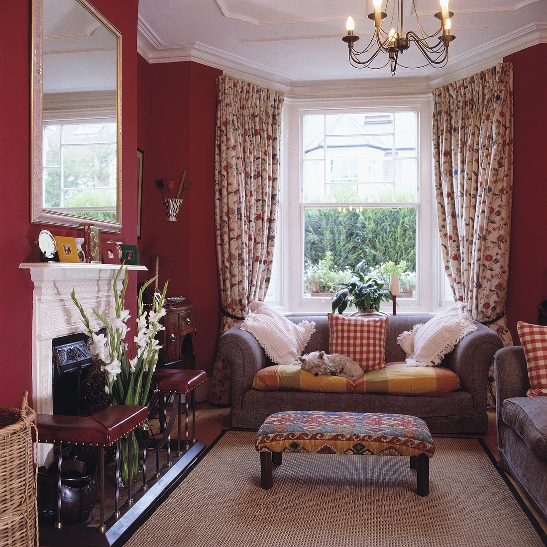 Traditionelles Wohnzimmer mit rot getönten Wänden und gepolstertem Hocker vor moderner Sofagarnitur im Erker