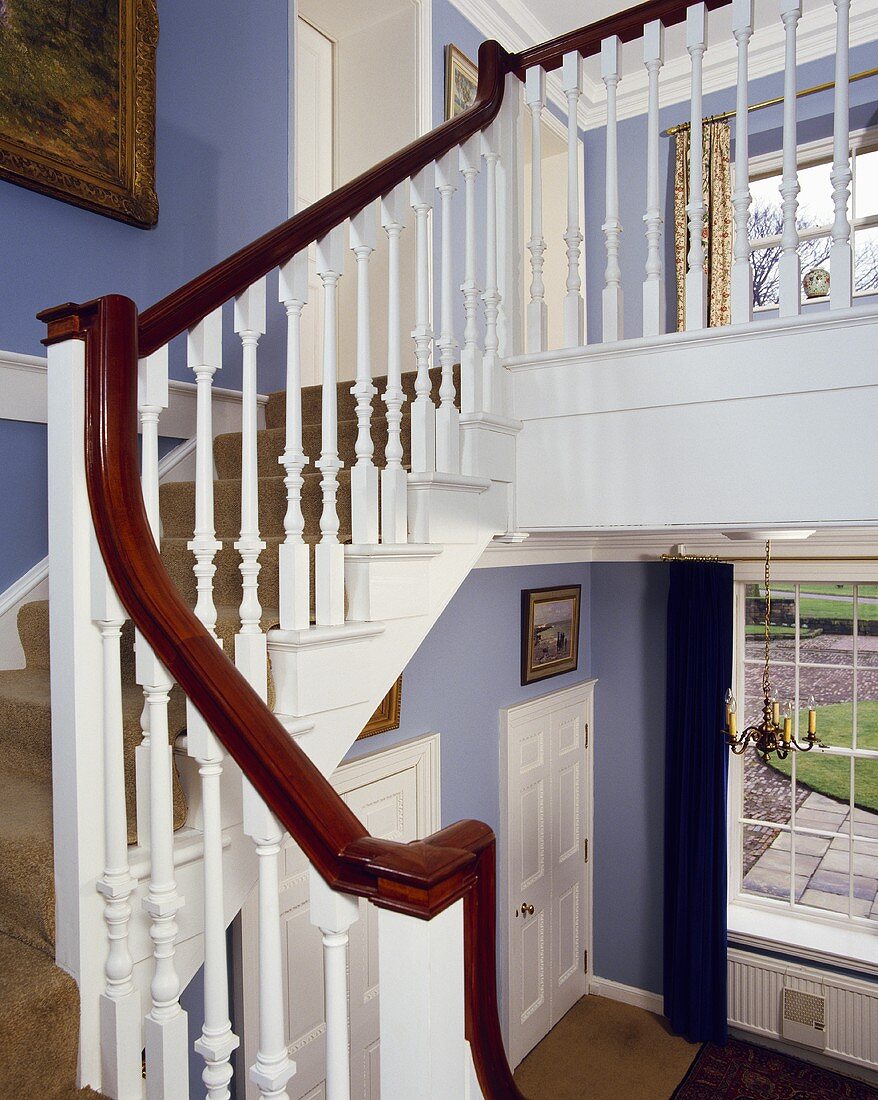 Weisses Treppengeländer mit Mahagoni-Handlauf in einer blauen Halle