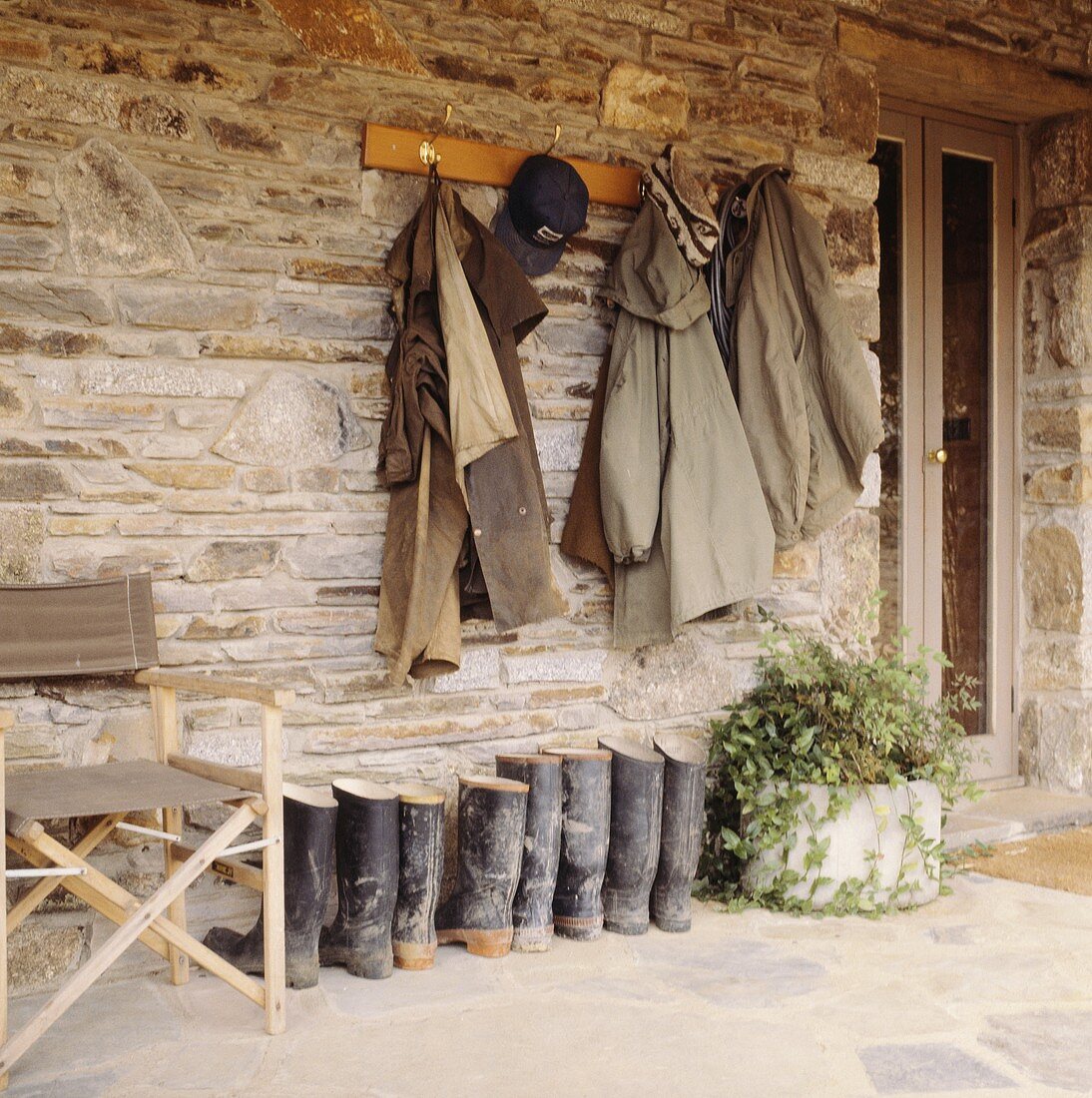 Mäntel hängen an der Steinmauer über Gummistiefel auf Veranda