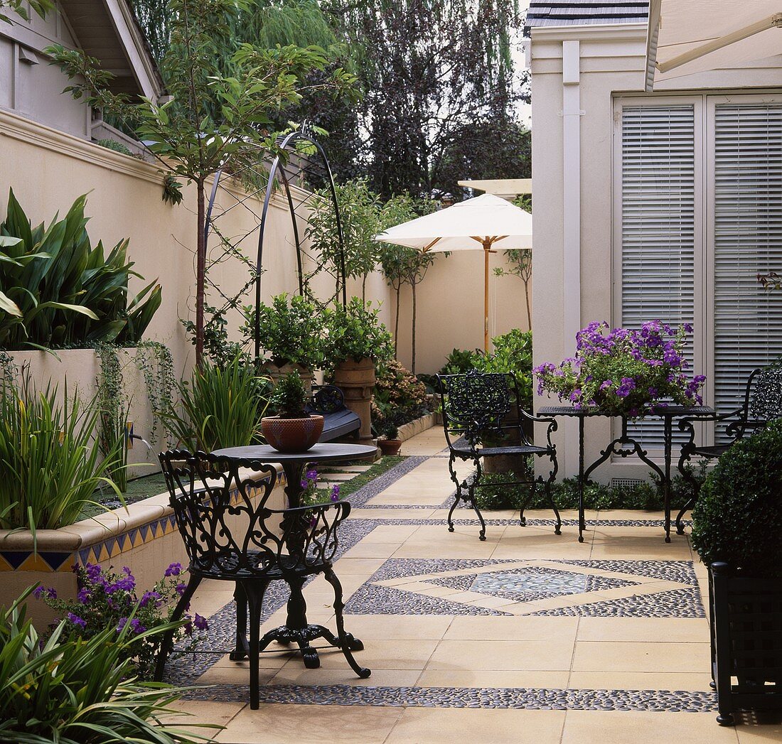 Möbel aus Metall auf gefliester und gepflasterter Terrasse in einem modernen Stadtgarten im Sommer