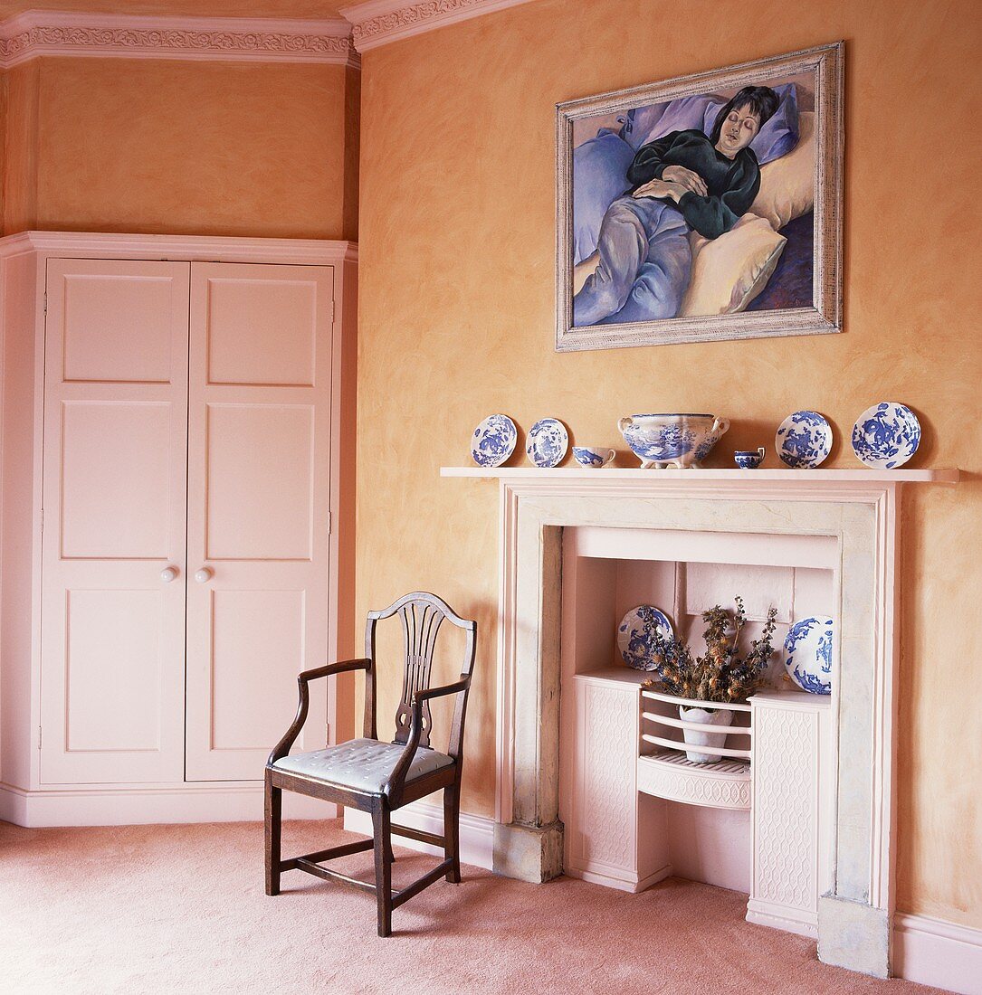 Altbauwohnraum mit apricotfarbenen Wänden mit weißem Kamin neben Stuhl und Einbauschrank