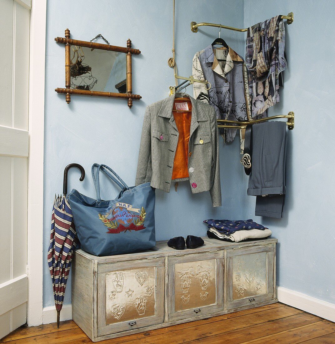 Kleidung auf Garderobe aus Messing auf pastellblauer Wand und alte bemalte Truhe