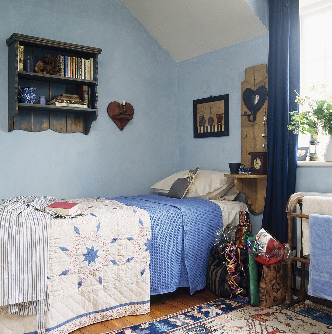 Einzelbett mit ländlicher Tagesdecke und blau getönte Wand im Dachzimmer