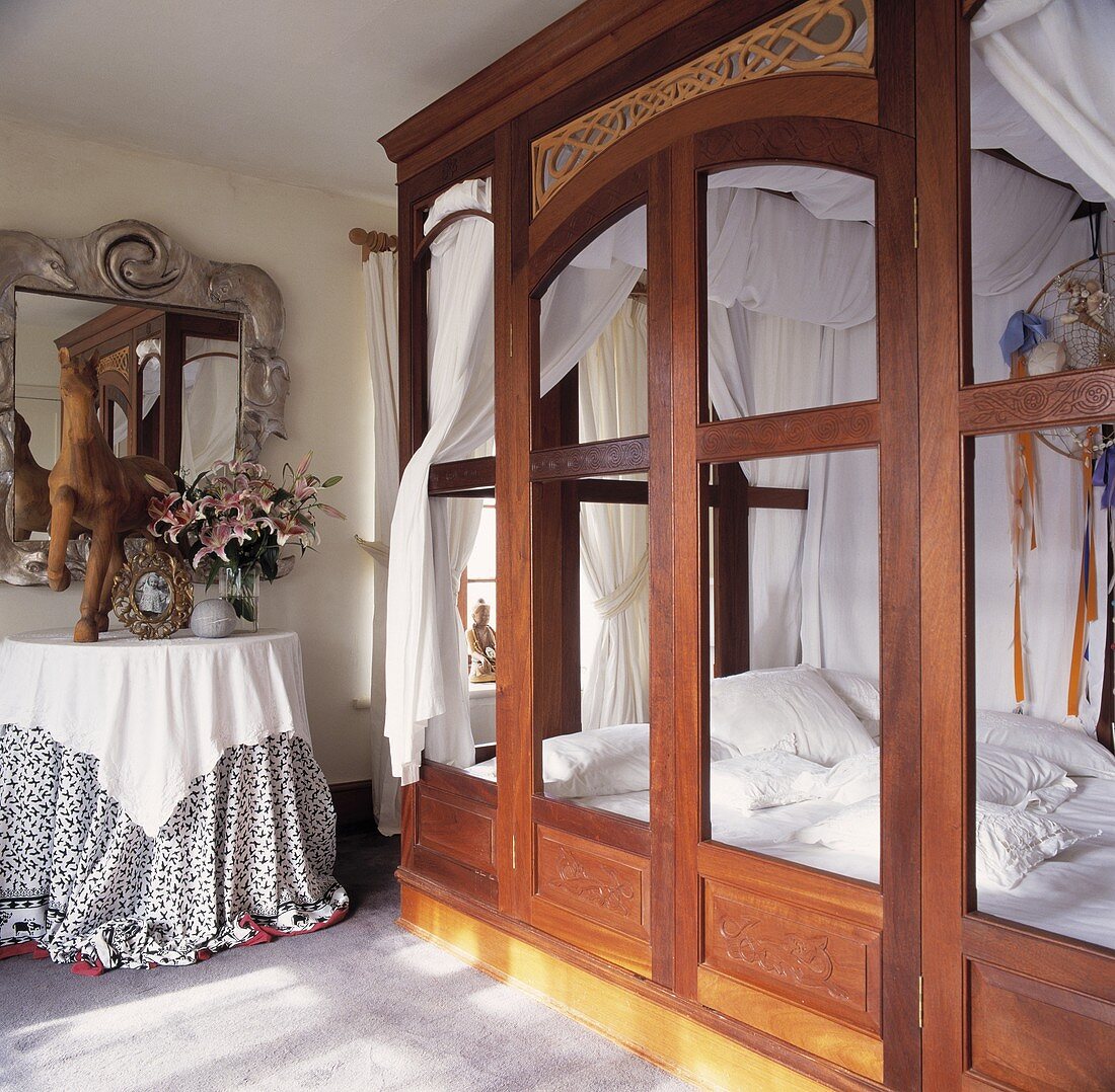 Bett mit weißer Bettwäsche hinter Holzeinbau mit Öffnungen