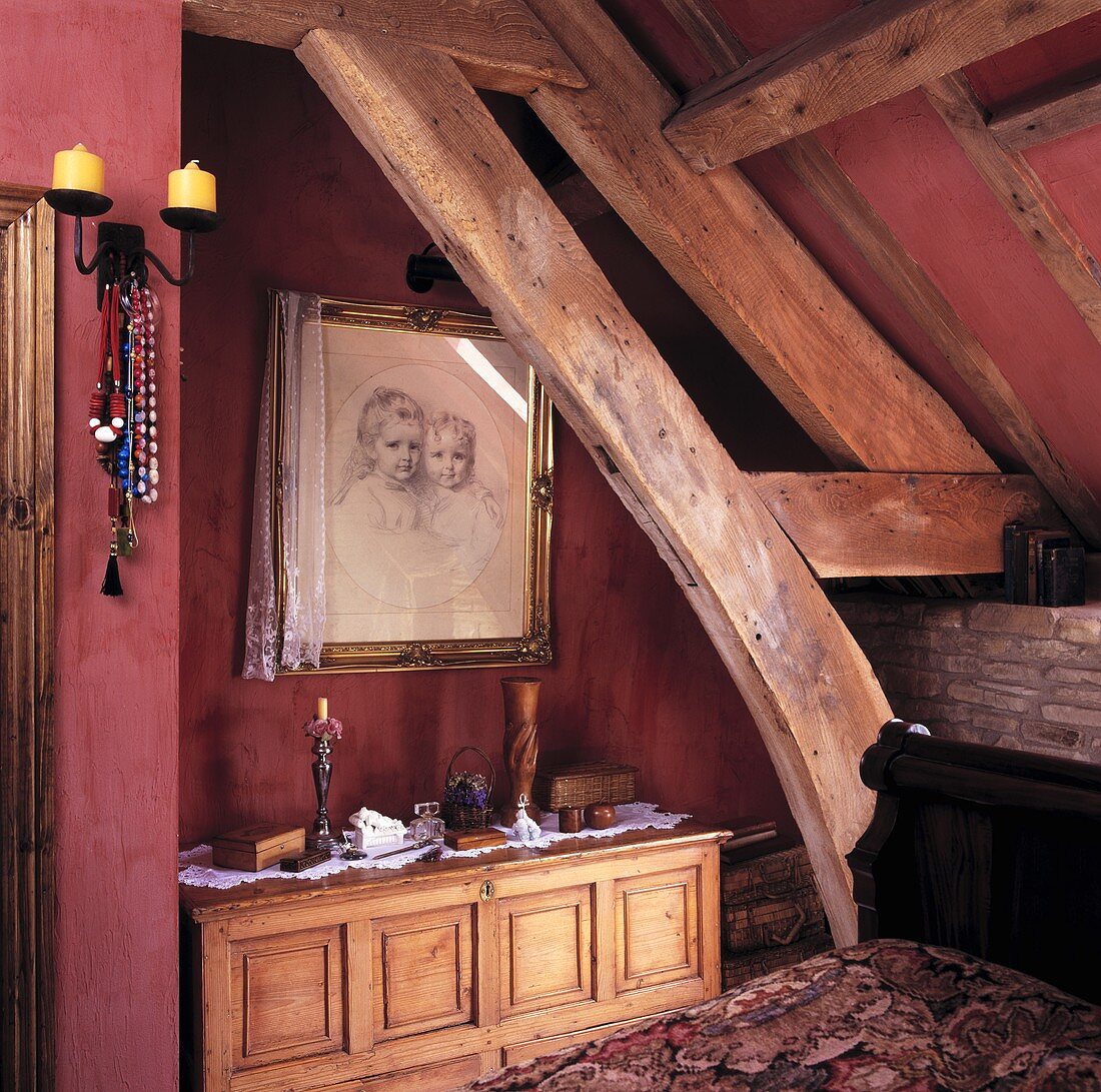 Altes Dachzimmer mit Holzkonstruktion vor roten Wänden und gerahmtes Bild über Holztruhe