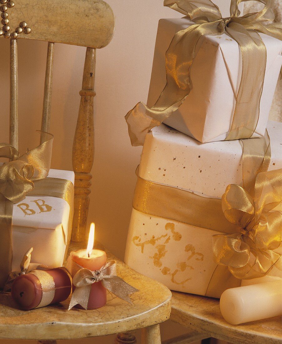 Weihnachtsgeschenke mit weißem Papier und goldenem Band auf rustikalem Stuhl mit Kerzenlicht