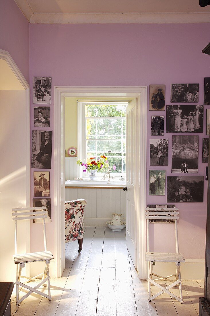 weiße Klappstühle vor rosa Wand mit Fotografien und offener Tür mit Blick ins Bad