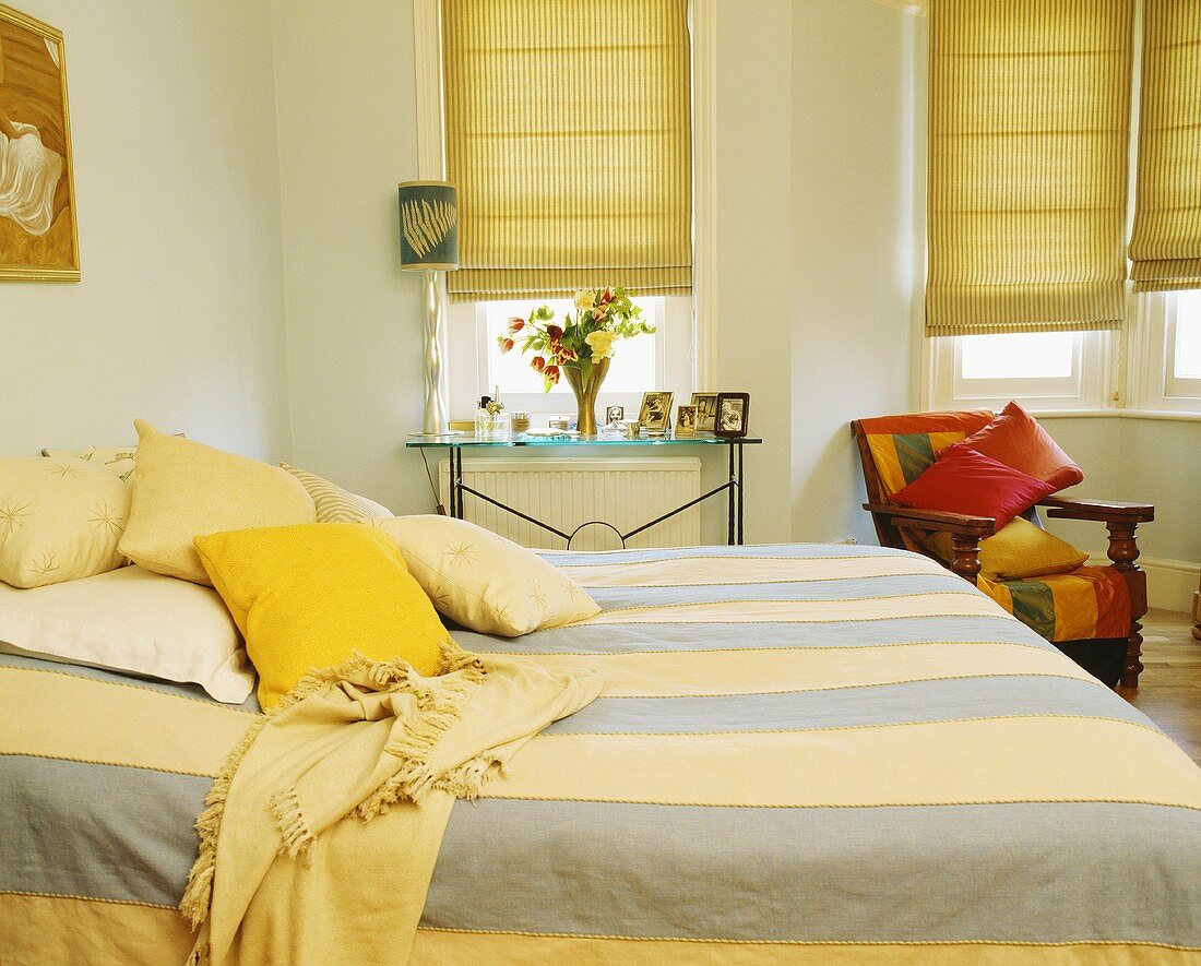 Doppelbett mit gestreifter Bettdecke und Rollos vor Fenster