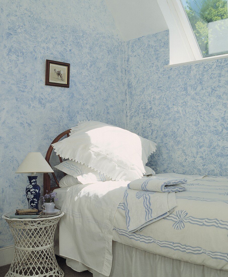 Ländliches Schlafzimmer mit weiß blauen Wänden und Nachttisch aus weißem Geflecht