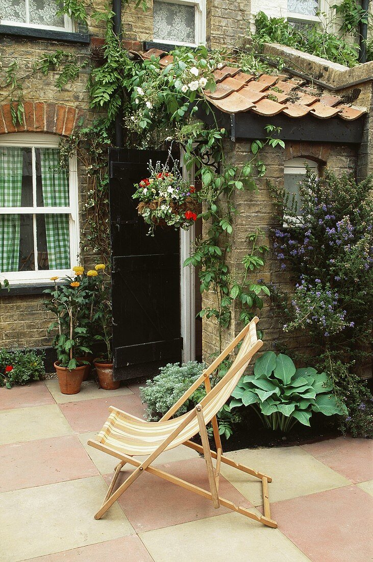 Liegestuhl auf Terrasse vor Haus mit Natursteinfassade