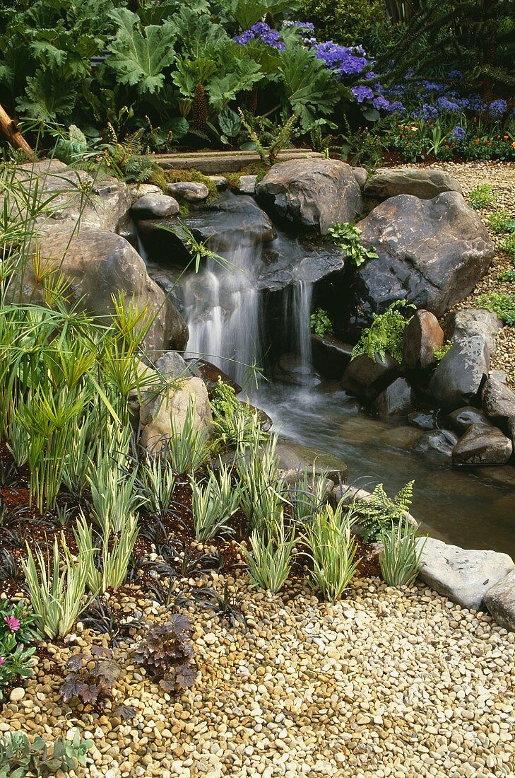 Wasserfall mit Felsböcken am Bach im blühenden Garten