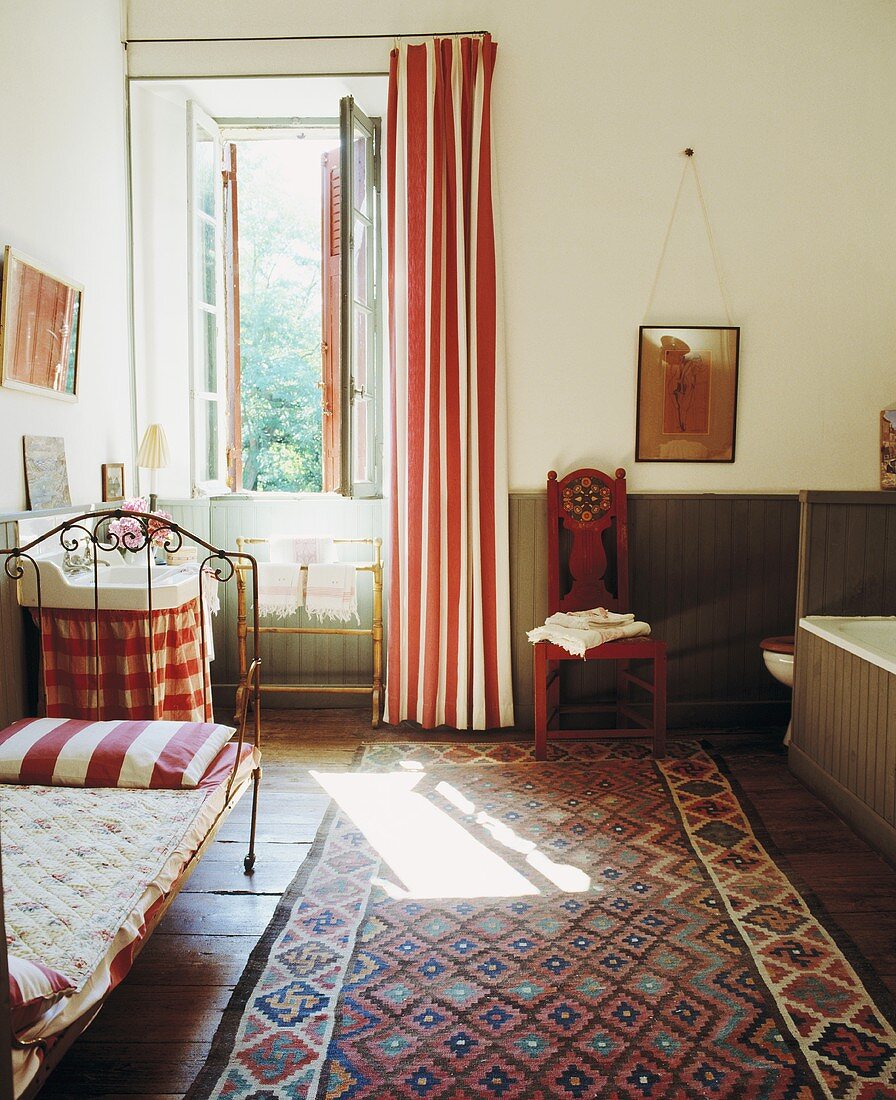 Traditionelles Gästezimmer mit gemustertem Teppich vor Bett und Waschtisch am Fenster