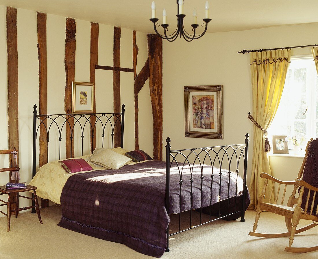 Traditionelles Schlafzimmer mit Bett aus antikem Metallgestell vor Holzbalkenwand