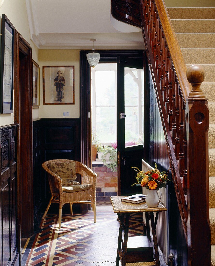 Korbstuhl neben offener Haustür im traditionellen Treppenhaus