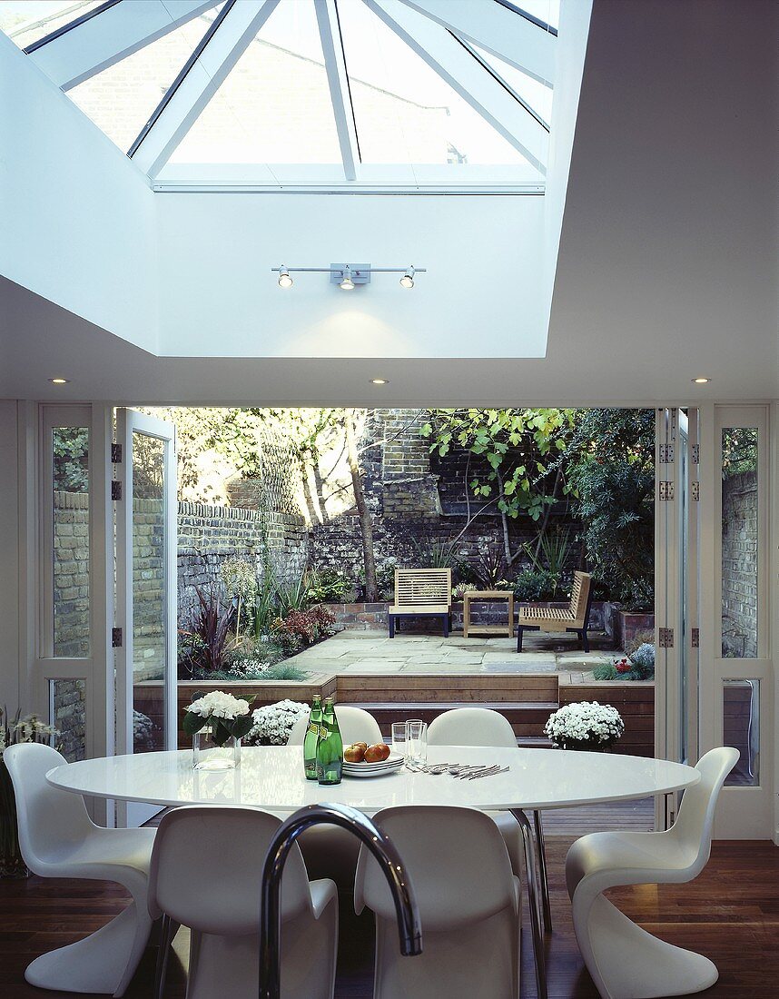 A dining table with white Bauhaus bucket chairs in front of open terrace doors