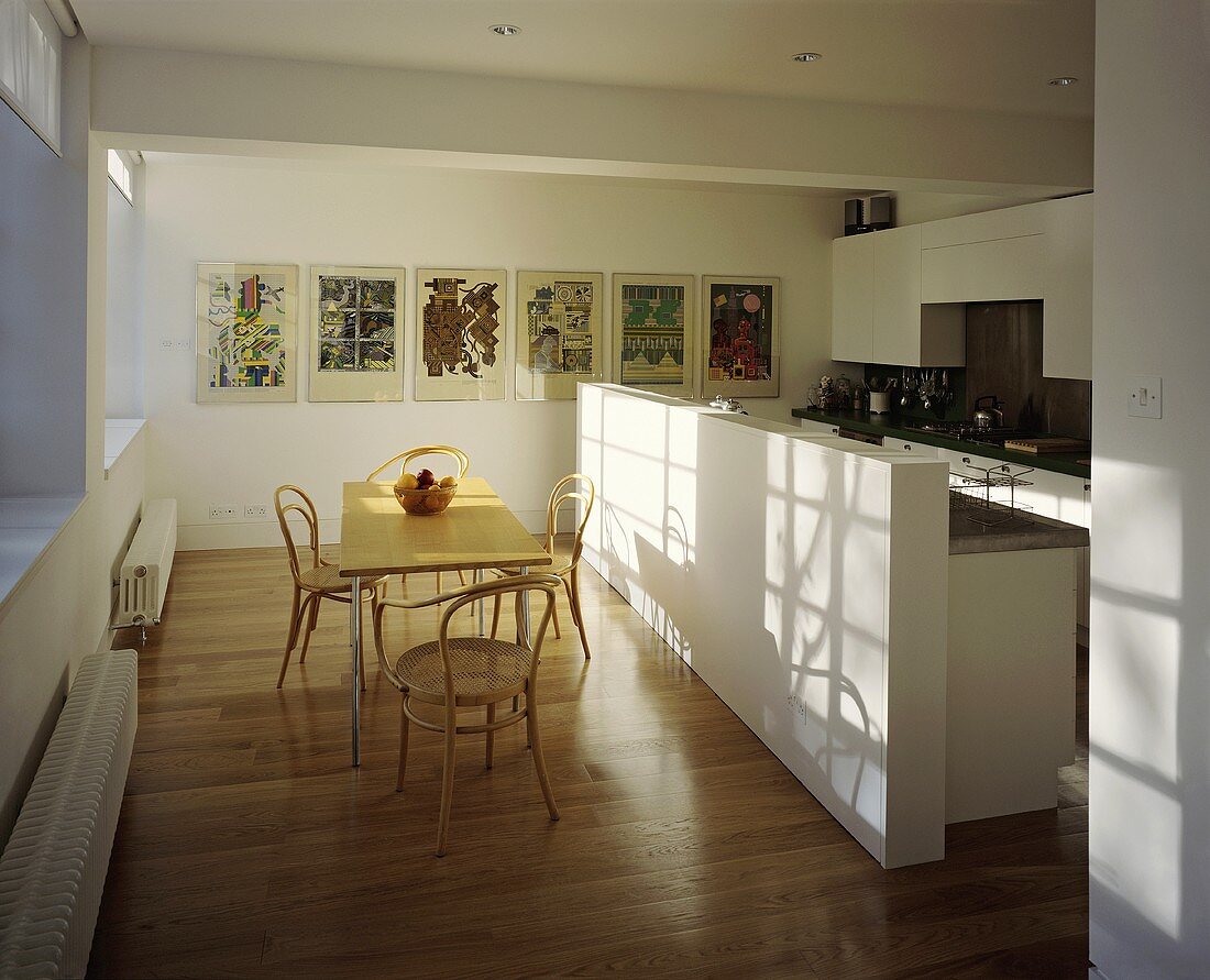 An open-plan kitchen with a dining table and Thonet chairs in front of a white kitchen counter