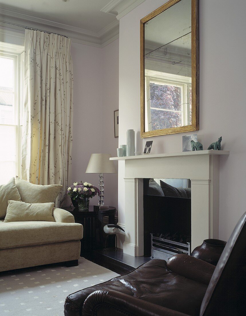 A brown leather armchair and a white sofa in front of a fireplace with a mirror above it