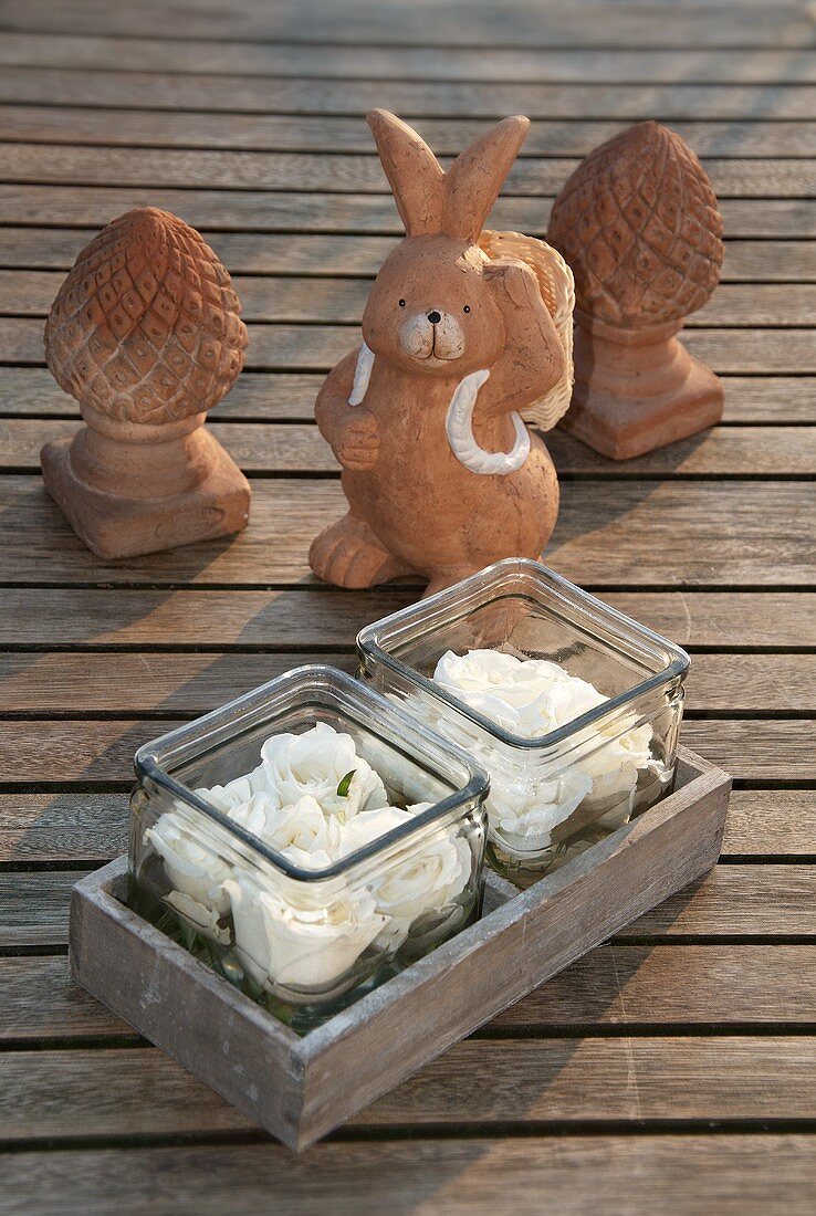 Roses in glasses with a clay rabbit figure on wooden boards