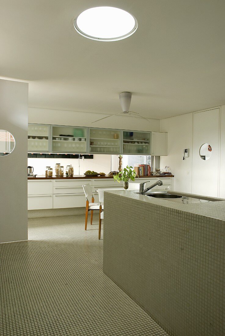 A white designer kitchen with a monolithic kitchen counter and mosaic tiles under a glass dome