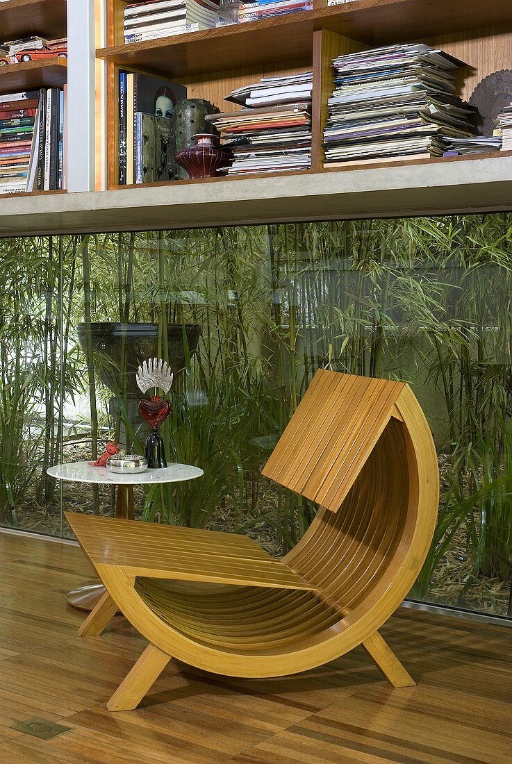 A wooden designer armchair in front of a window with a view of a courtyard filled with plants