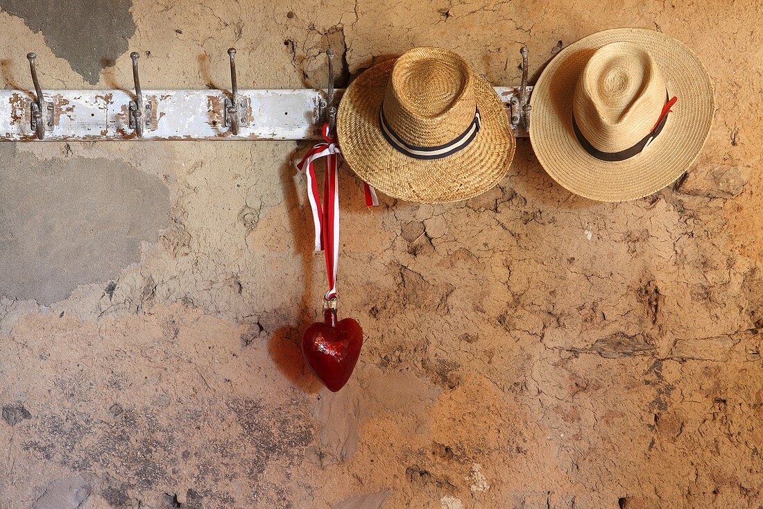 Strohhüte und ein Herz aus Glas auf einer alten Garderobenleiste