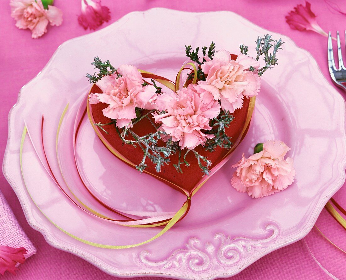 Gesteck aus rosa Nelken und Stacheldrahtpflanze in einem roten Herz