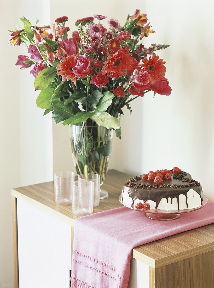 Schokoladentorte mit Sahne und Himbeeren neben Blumenstrauss