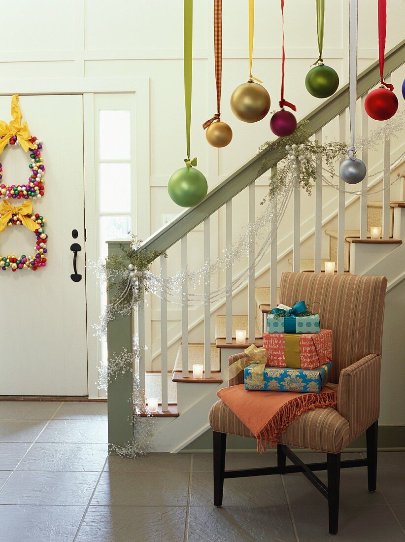 Geschenke auf Polsterstuhl neben Treppenaufgang auf weihnachtlich dekoriertem Flur