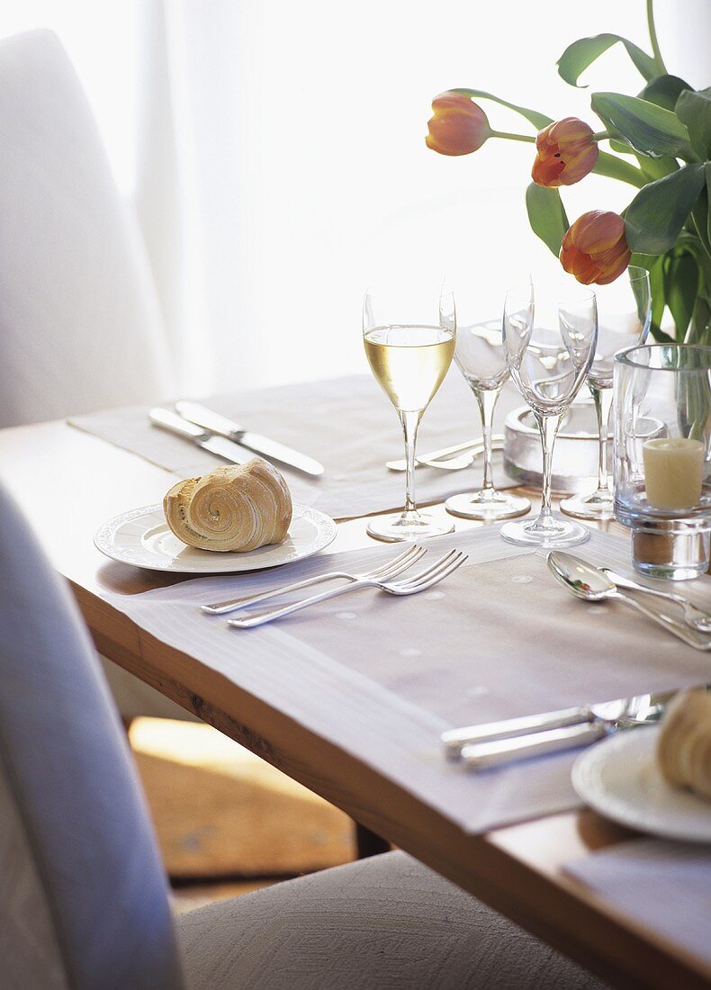 Gedeckter Tisch mit Hefegebäck, Weißwein und Tulpen