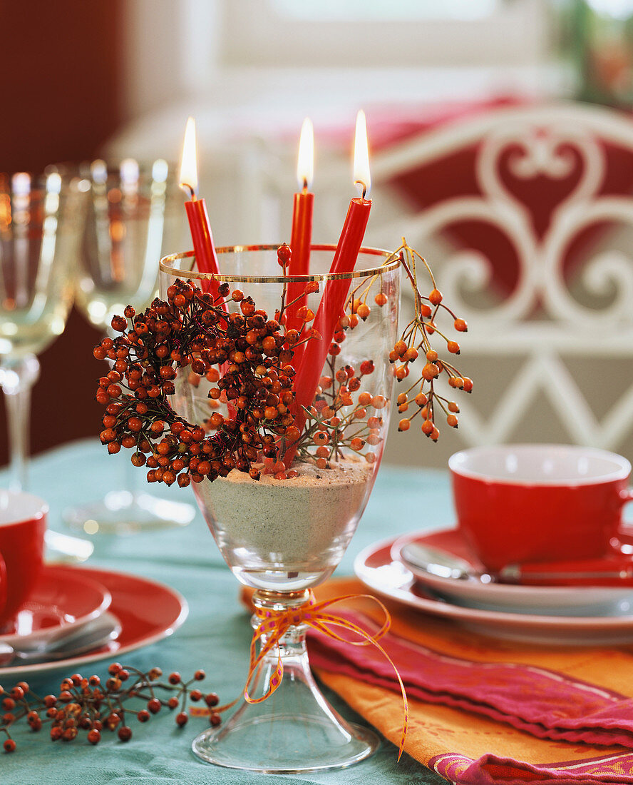 Rote Kerzen in einem Weinglas mit kleinem Hagebuttenkranz