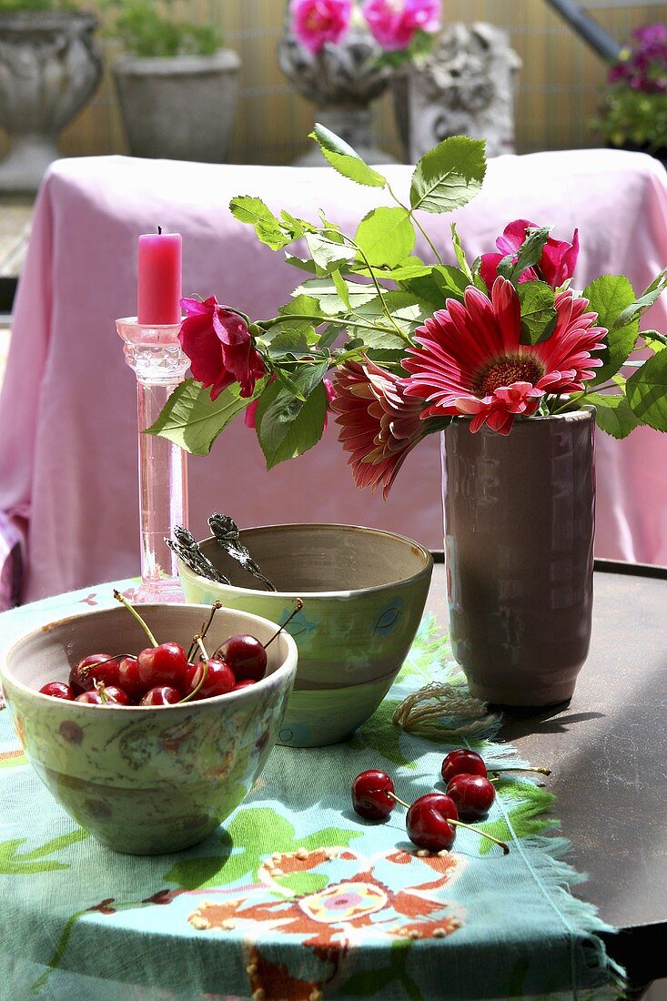 Ein Schälchen Kirschen mit Blumenvase auf einem Tisch