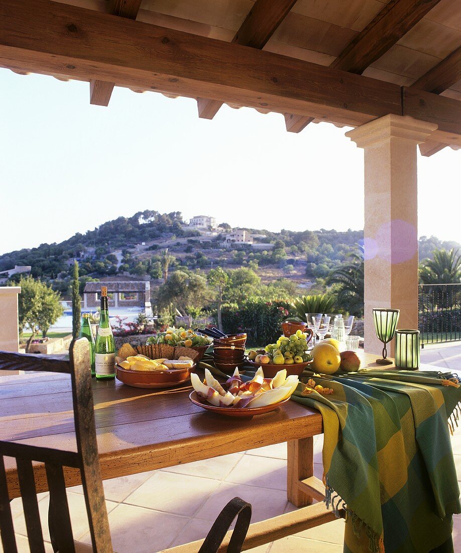 Gedeckter Tisch mit Antipasti auf überdachter Terrasse mit Blick auf mediterrane Landschafr