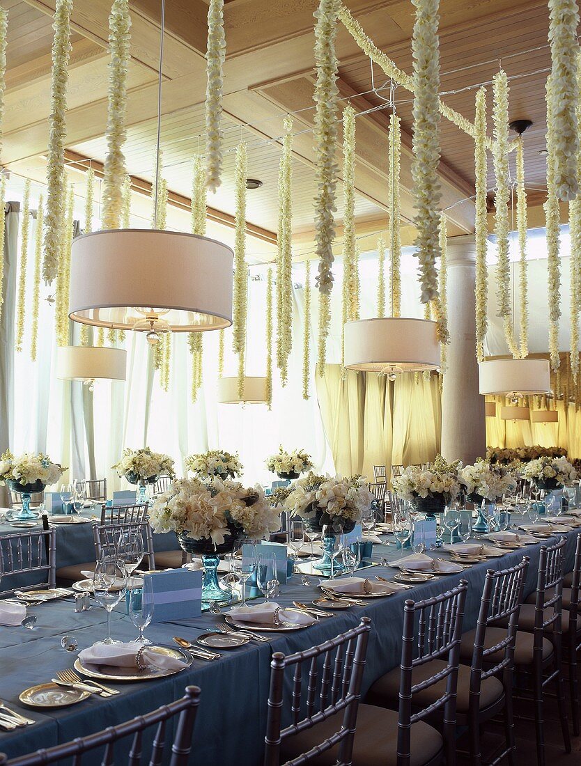 Festlich gedeckte Hochzeitstafel in Saal mit weisser Blumendeko auf Tisch & an Saaldecke