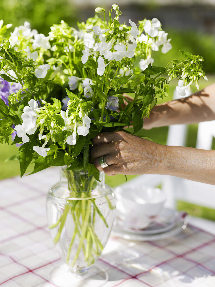 Arranging flowers on table laid for coffee in garden